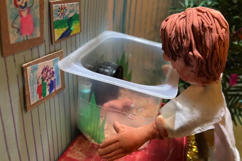 Scene of a man made of clay looking into a plastic container representing an aquarium