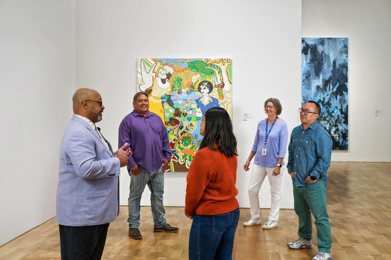 Museum guests listen to a museum guide as they stand in front of On Duty, Not Driving by Milwaukee-born artist Reginald Baylor.