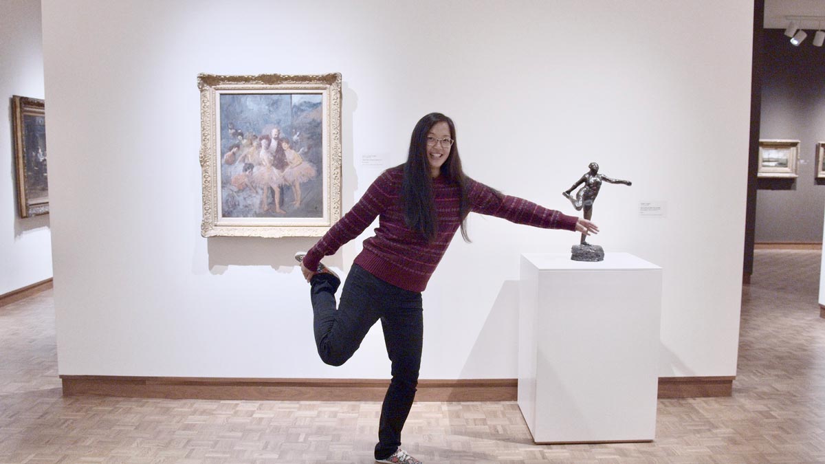 Young woman mimicking the pose of a sculpture next to her