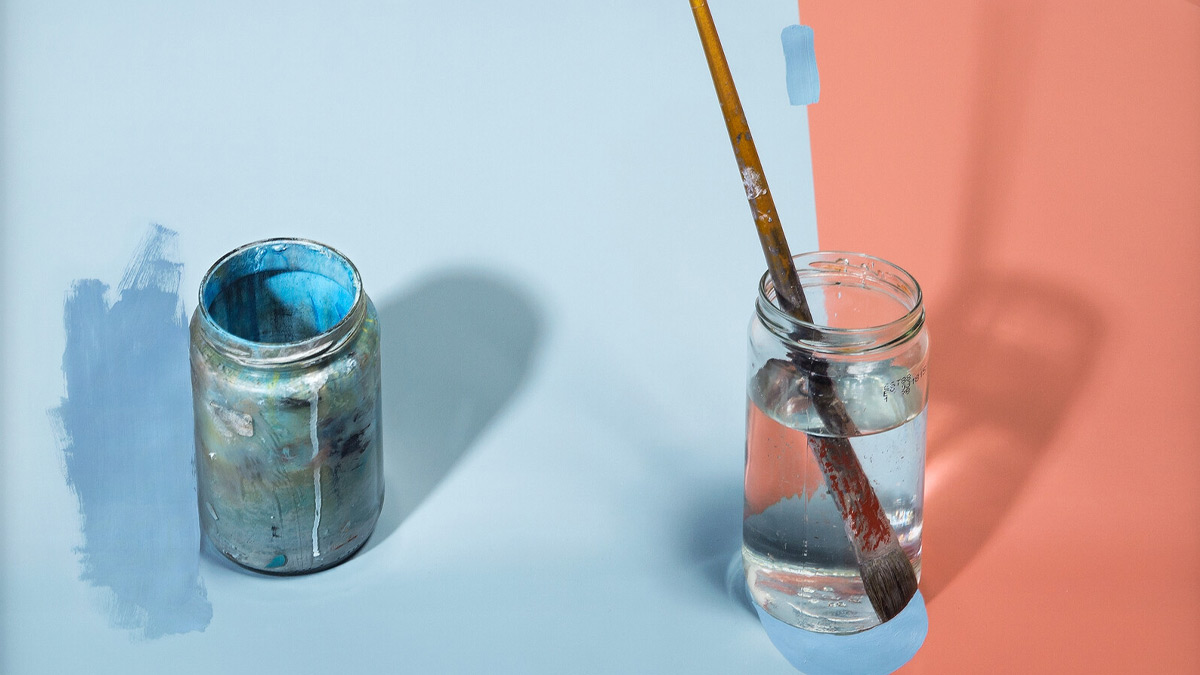 Glass of water with paintbrush next to a painting of a jar covered in paint