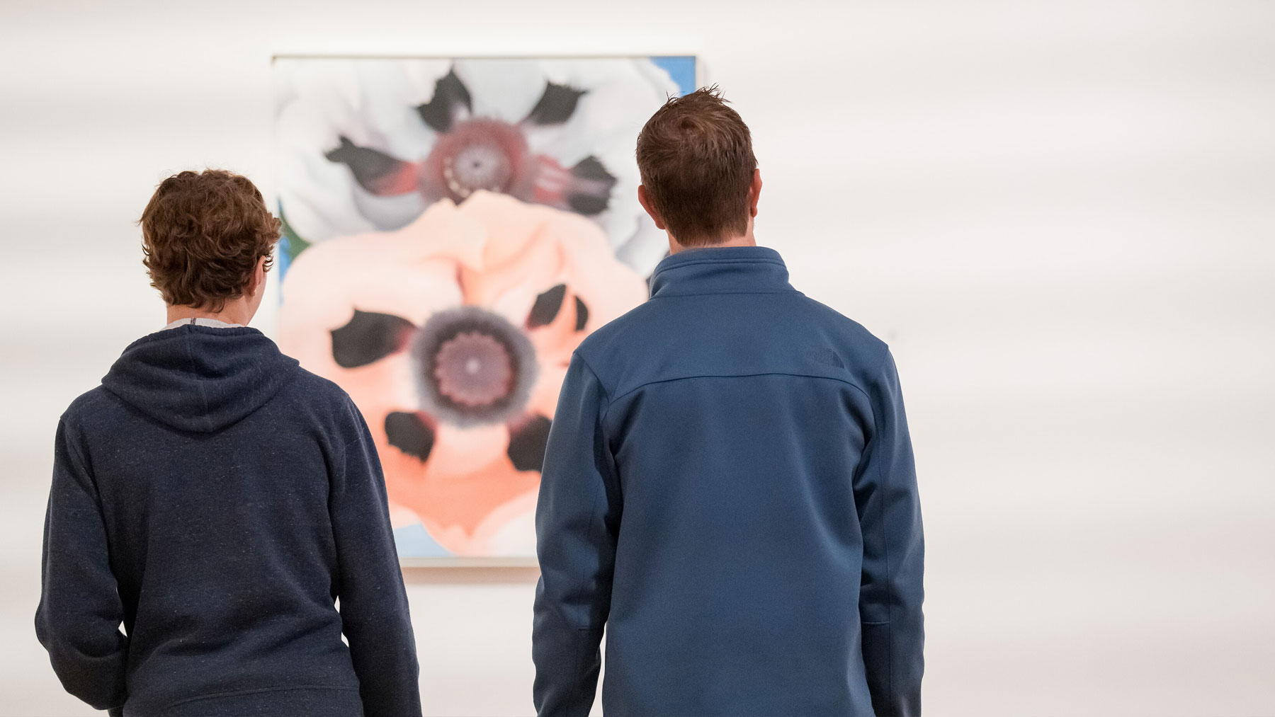 A man and a teenaged boy looking at a work of art by Georgia O'Keeffe
