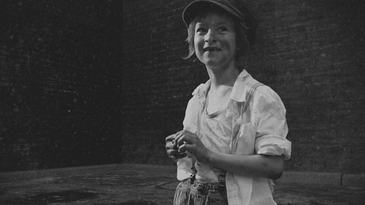 Black and white photograph of a young child in baggy clothes and a cap