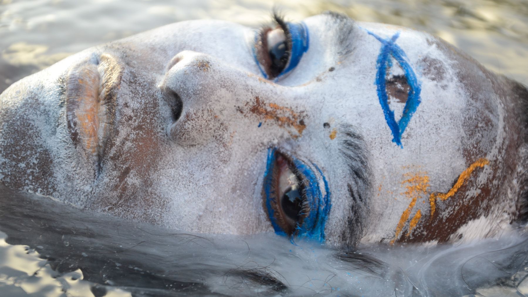 Person floating in water with white and blue face paint