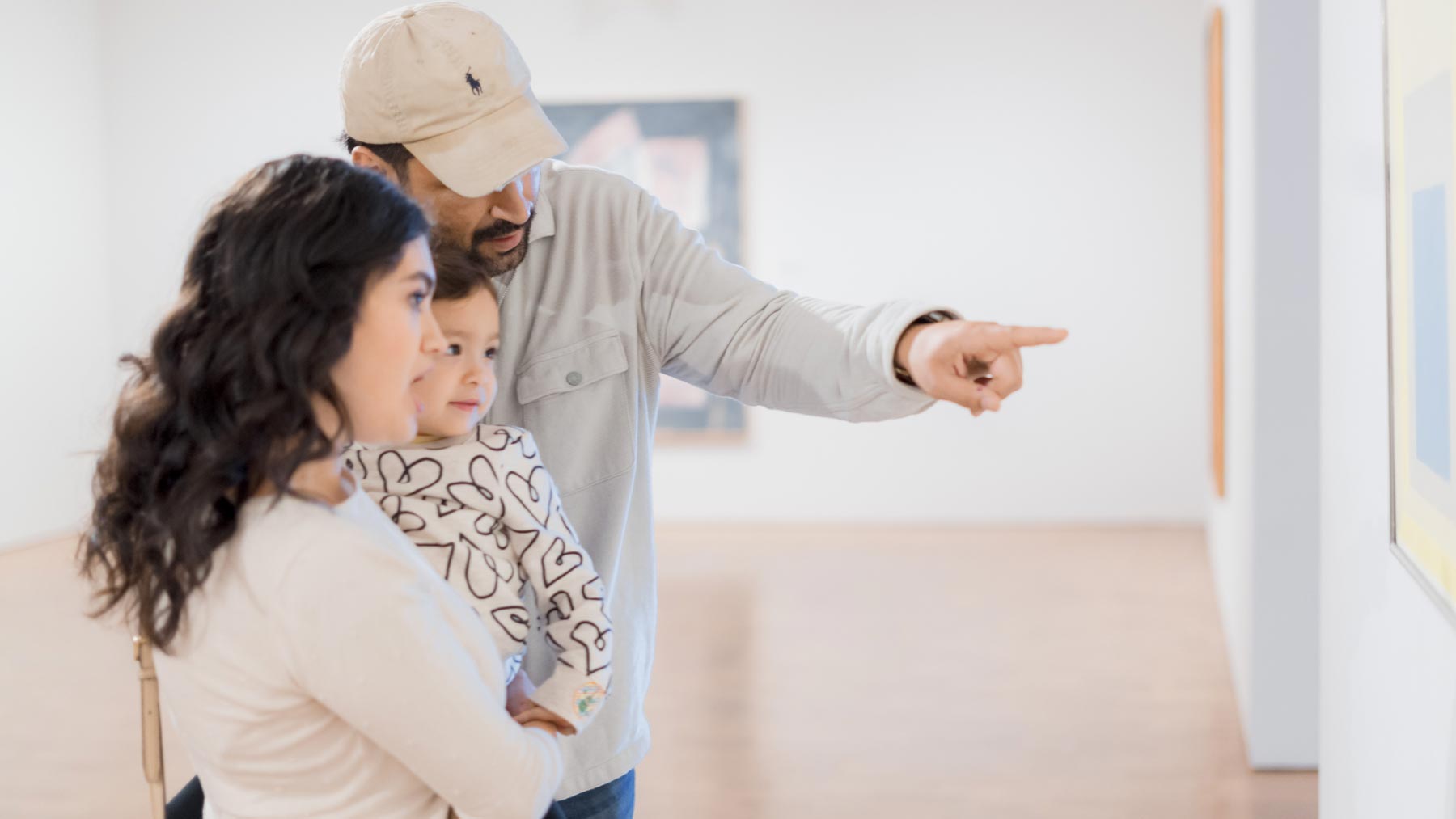 Mother and father holding their young daughter and pointing at a work of art