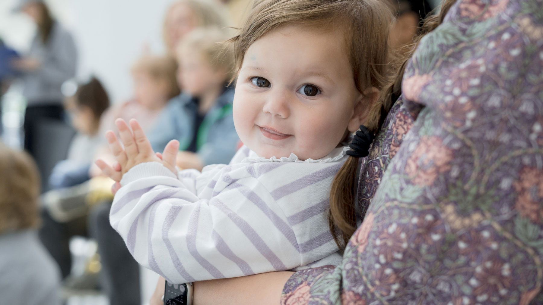 Small child in their mother's arms smiling at the camera