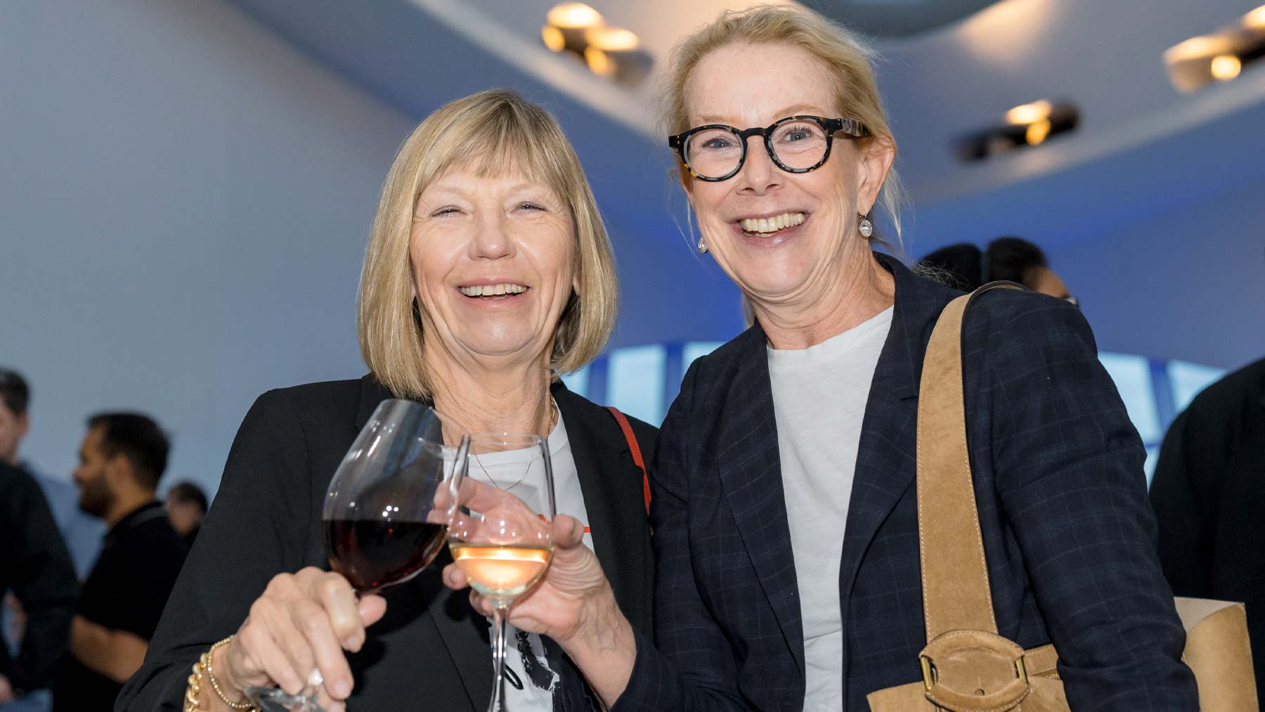 Two women in nice attire holding wine.