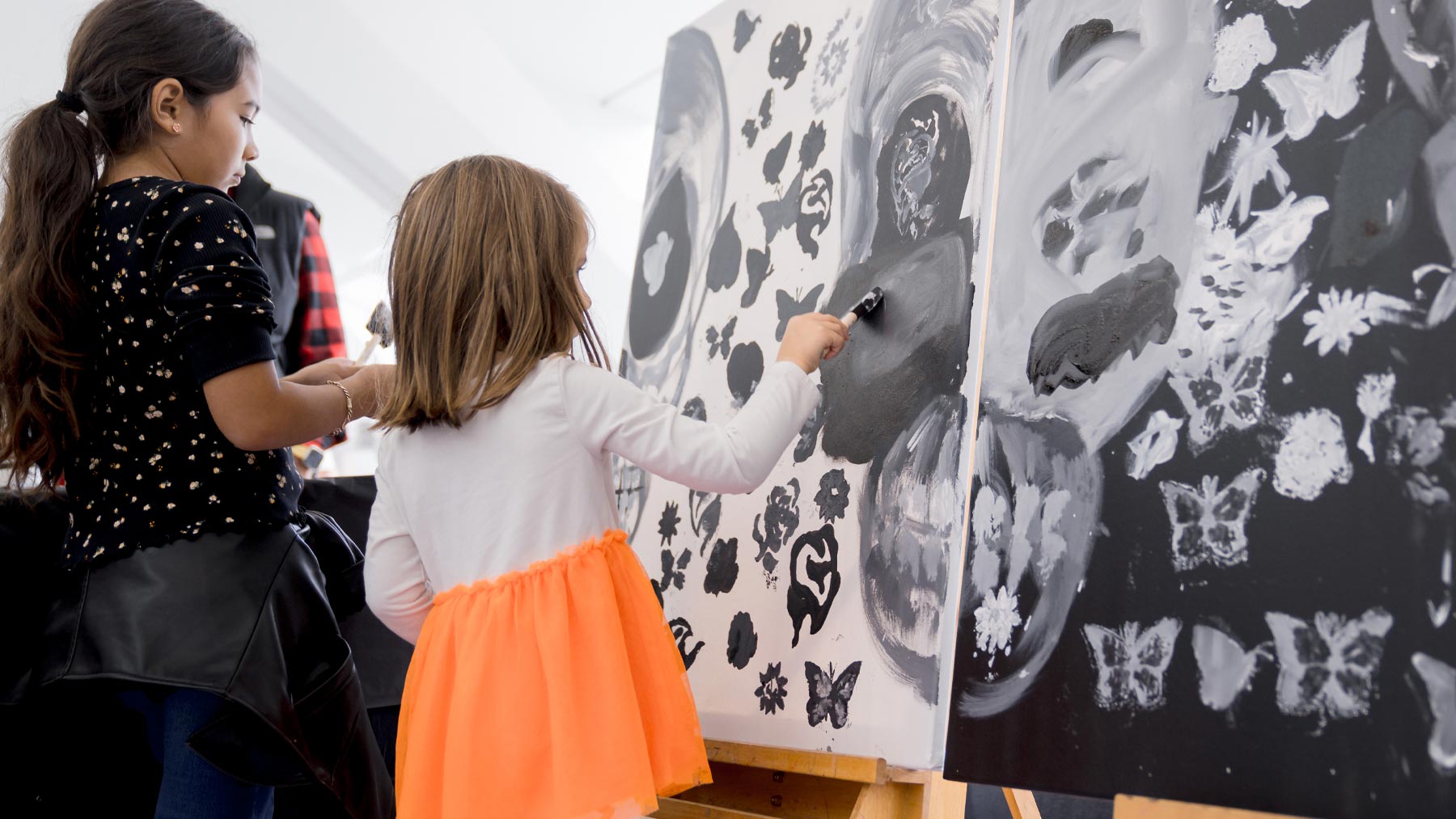 Two young girls painting on a communal black and white mural