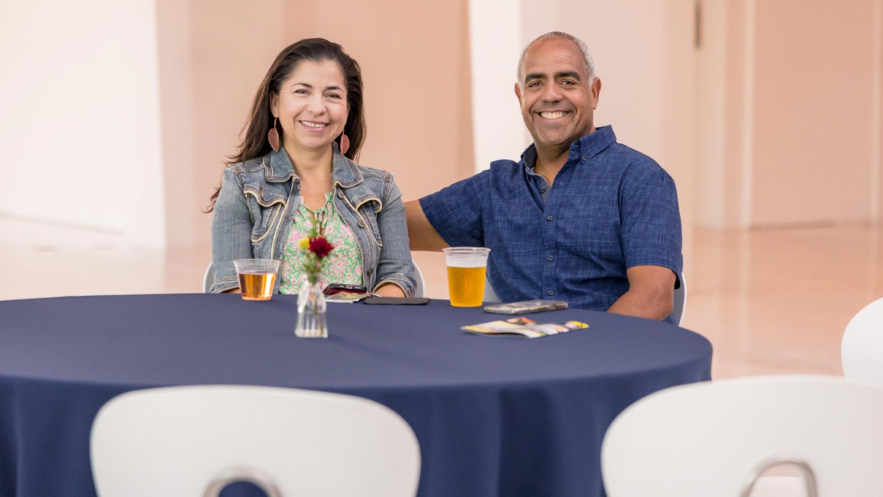 Man and woman smiling and sitting at a table with white chairs and a blue tablecloth
