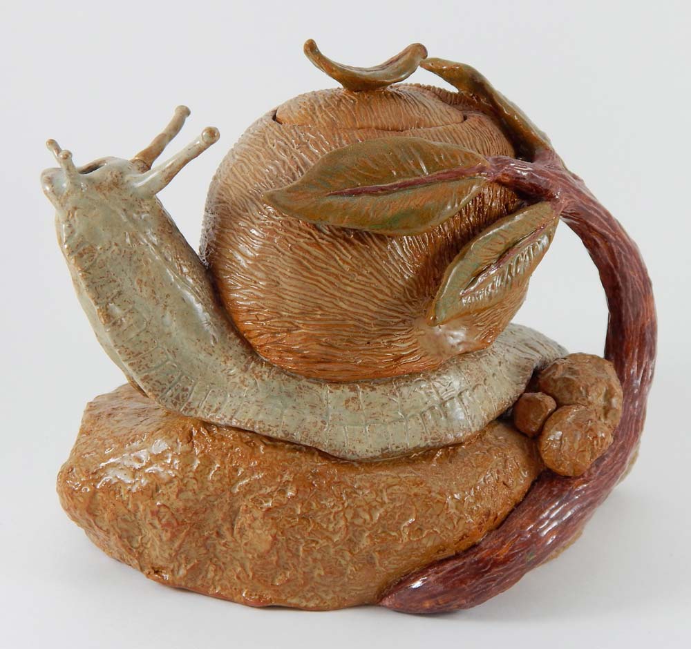 Ceramic teapot in the shape of a snail wrapped in a branch with leaves sitting on a stone
