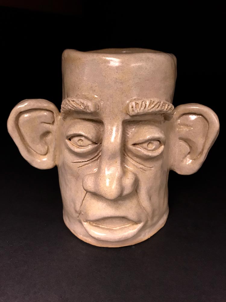 Tan, ceramic sculpture of a face with large ears and nose