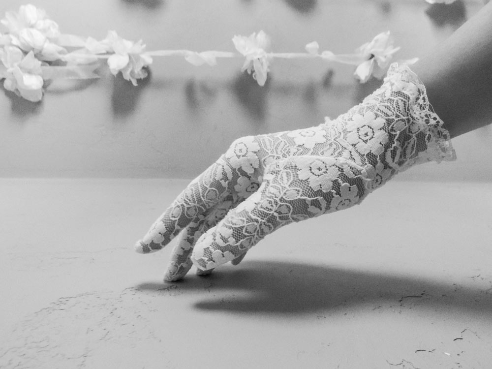 A hand with a white lace glove touching the surface of a table