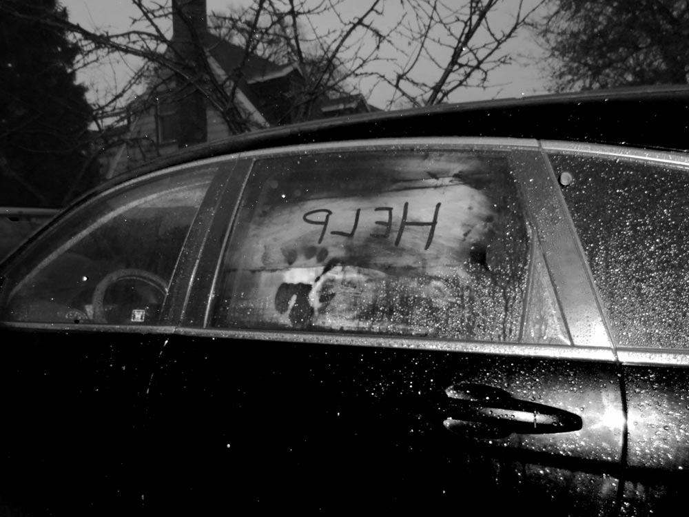 Older black car with help written in the condensation on the window and a handprint