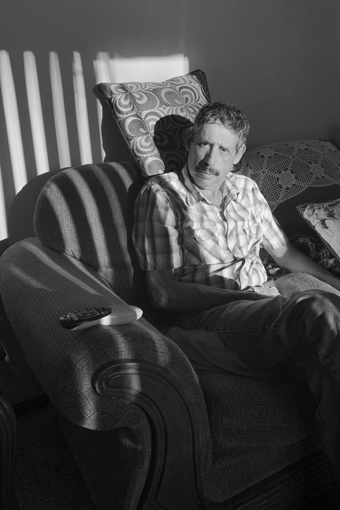 Older man sitting on a couch looking at the camera through a striped shadow