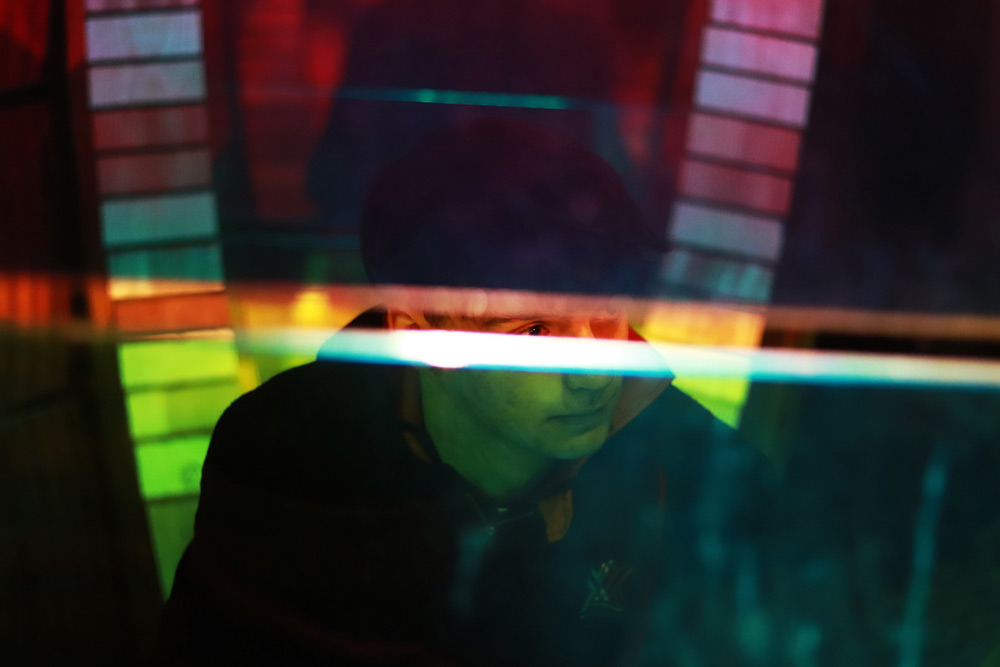 Young man looking to the side behind a transparent wall of colored glass with a crack through the middle