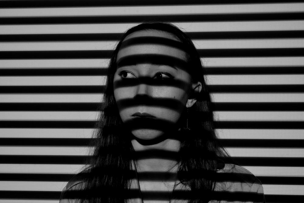 Young woman from the shoulders up with the shadows of blinds on her face