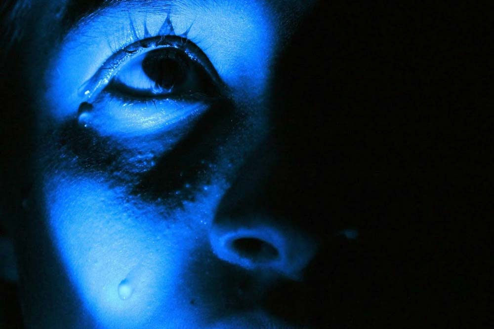 Blue-toned girl zoomed in on an eye with a tear on her cheek