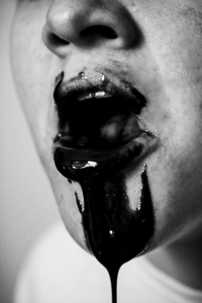 Closeup of a person's open mouth with black liquid dripping out
