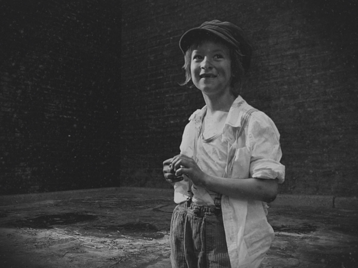 Black and white photograph of a young child in baggy clothes and a cap