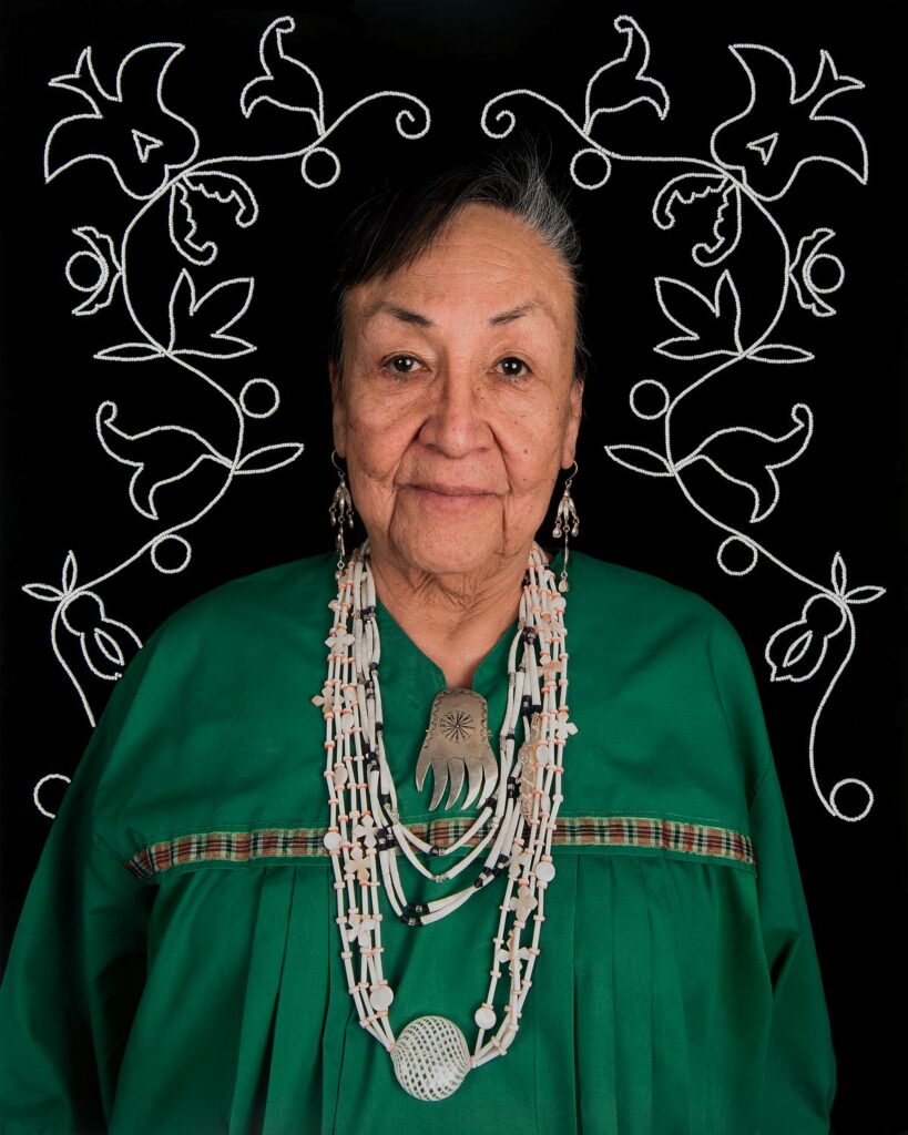 Older Native American woman in a green blouse and long necklace