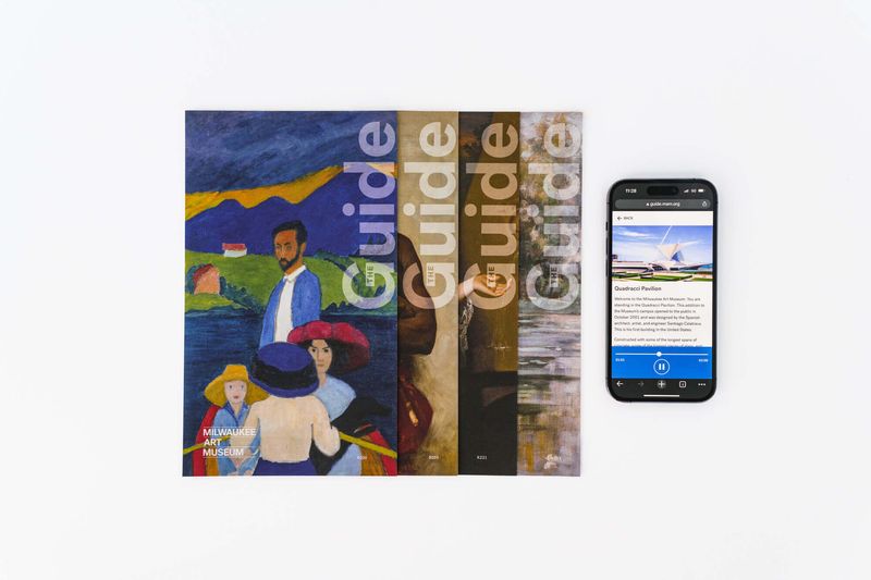 A stack of four museum collection guides sit to the left of a phone playing an audio guide. 