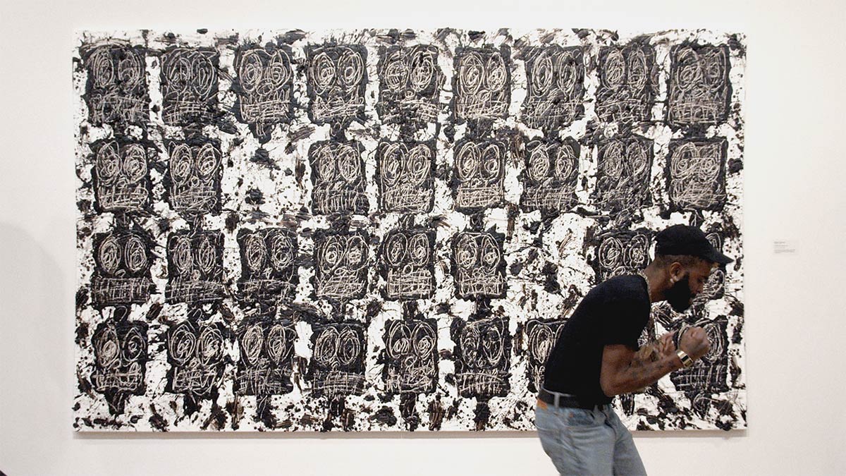 Man talking into a mic in front of Untitled Anxious Audience by Rashid Johnson