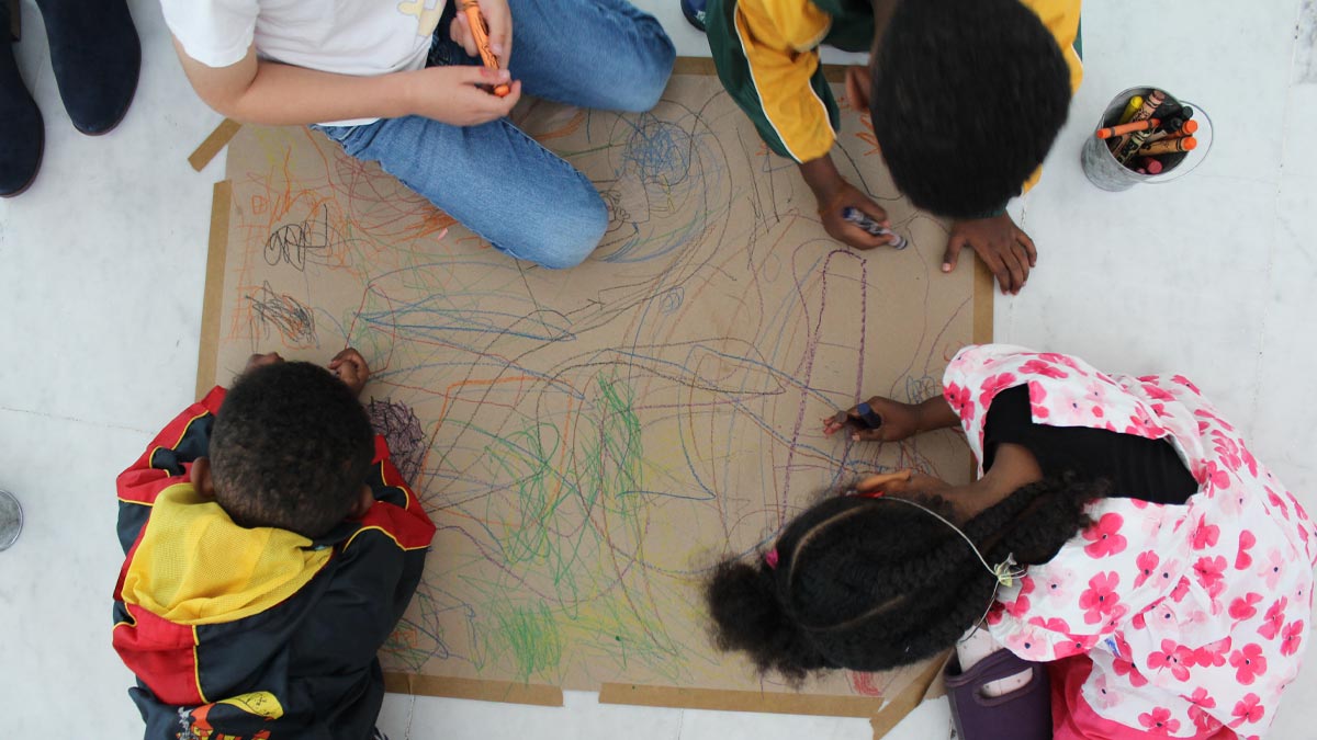 Birds eye view of four children drawing on a piece of cardboard