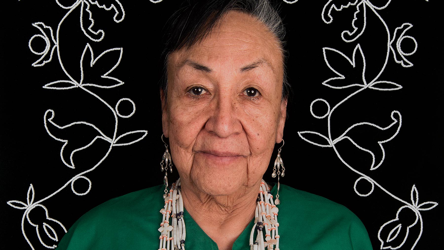 Older Native American woman with long earrings and a green blouse