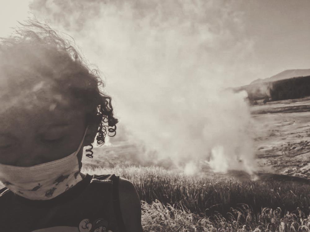 Young girl looking down with a mask on with grass burning in the background
