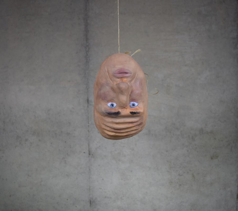 Face mask of a man hanging upside down with blue eyes, a bald head, and thick eyebrows