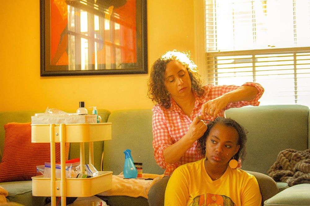 Young woman sitting down while her mother braids her hair