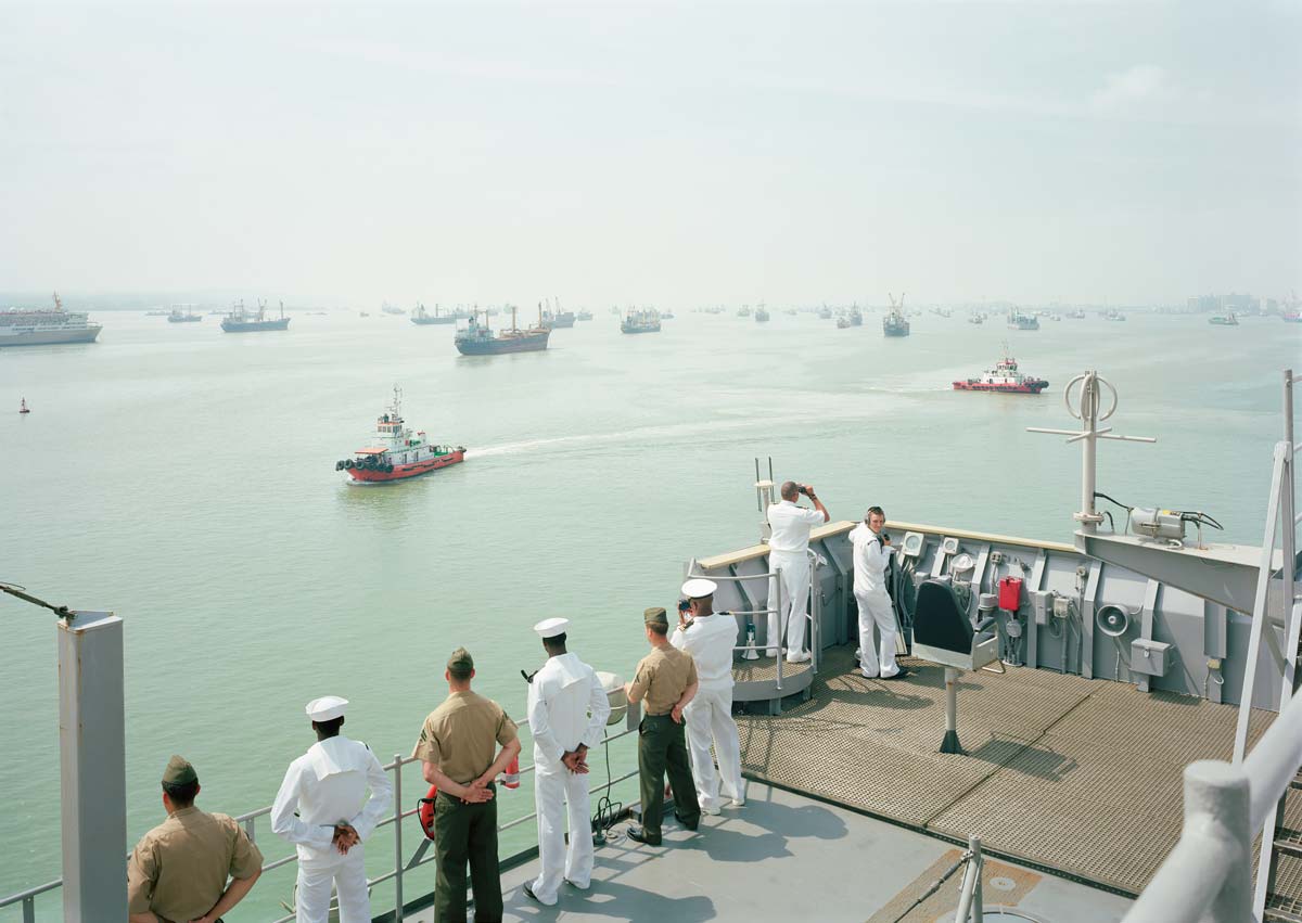 Uniformed men on a ship standing along the edge a boat looking out at other boats at sea
