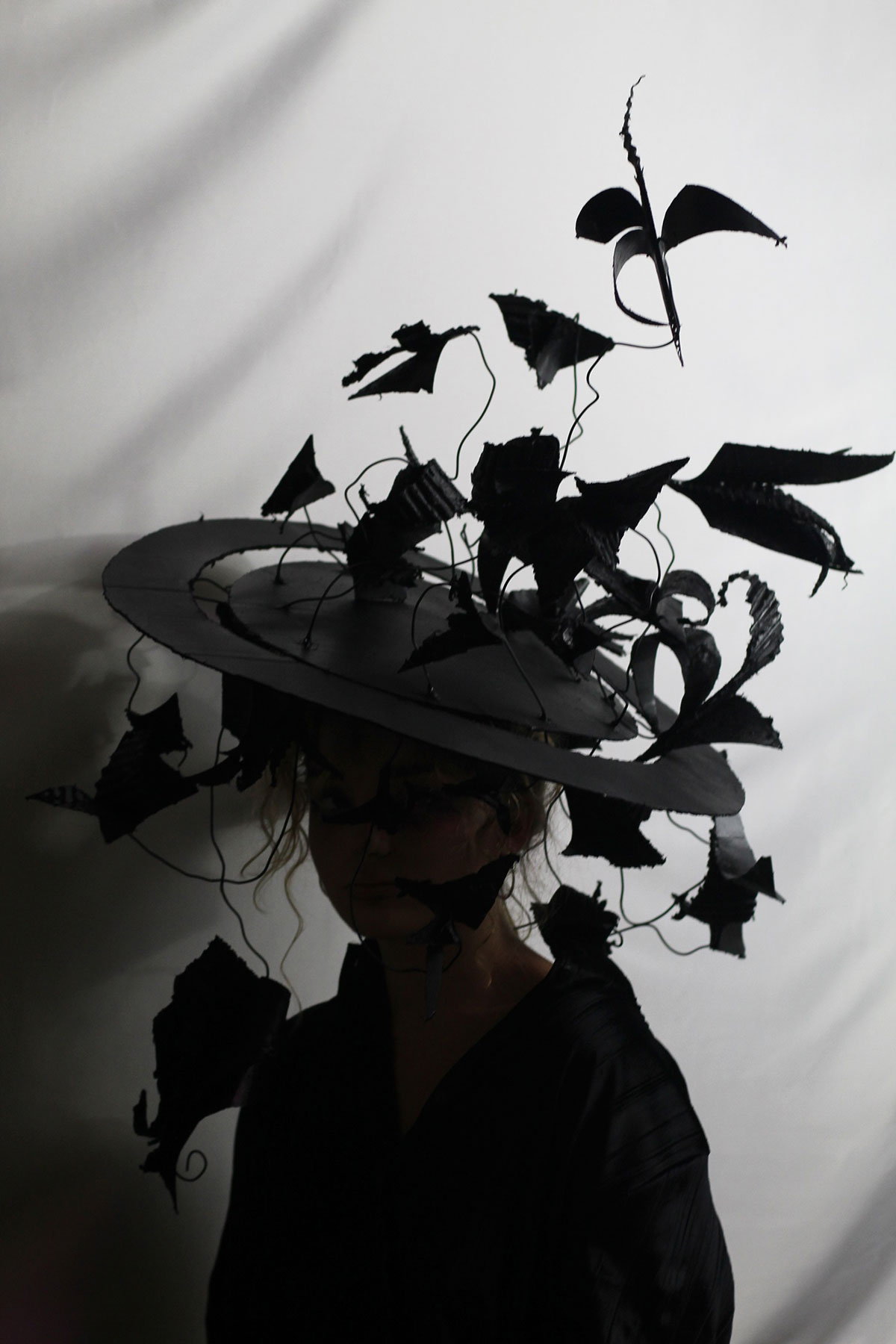 A woman wearing a black hat with a veil of leaves and crows and leaves on top